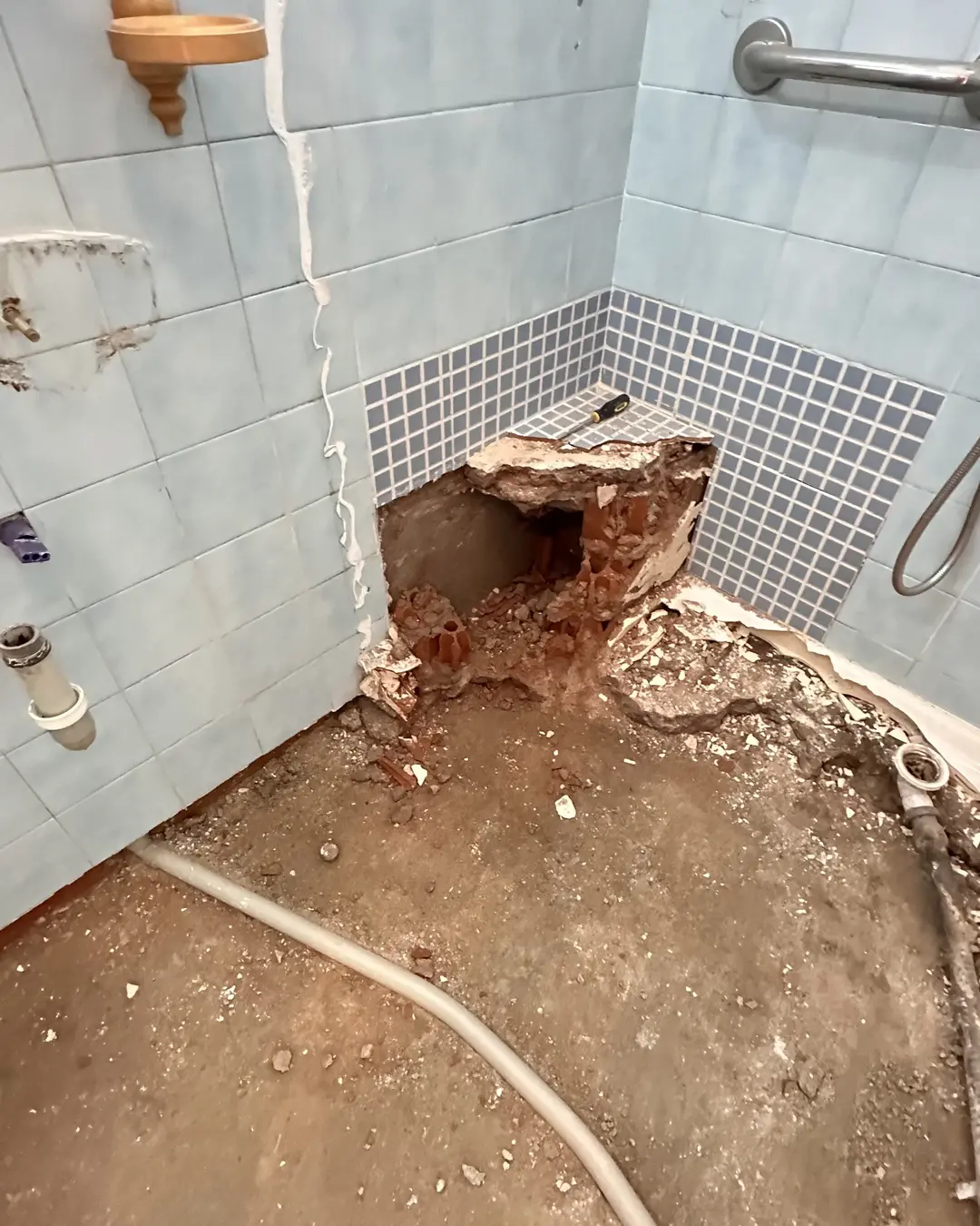 Rincón del baño durante la demolición de la bañera, con el suelo levantado y la pared abierta